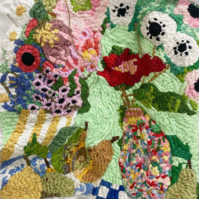 Hand embroidered textile landscape filled with flowers, plants and small figures