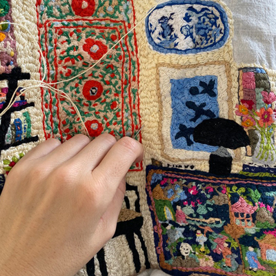 Embroidered textile scene with furniture, objects and decorative motifs
